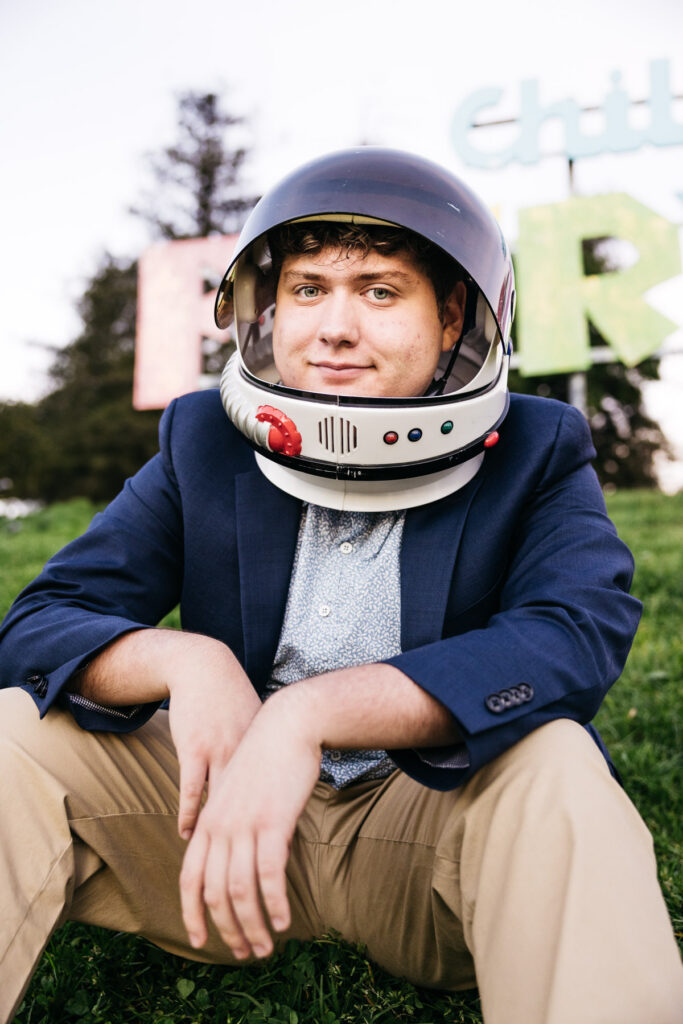 Senior grad is sitting on the lawn in front of the infamous Fairyland sign at Lake Merritt during a family photo session.