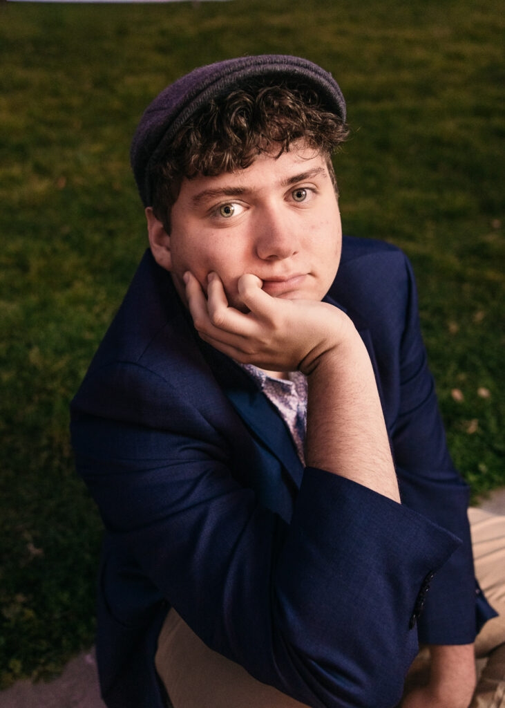 Senior is sitting on the grass with his chin resting on his hand during a family photo session at Lake Merritt.