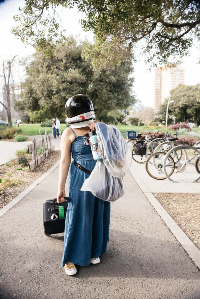 Mom is wearing her son's astronaut helmet and pulling a luggage full of props to her son's senior photo session at Lake Merritt.