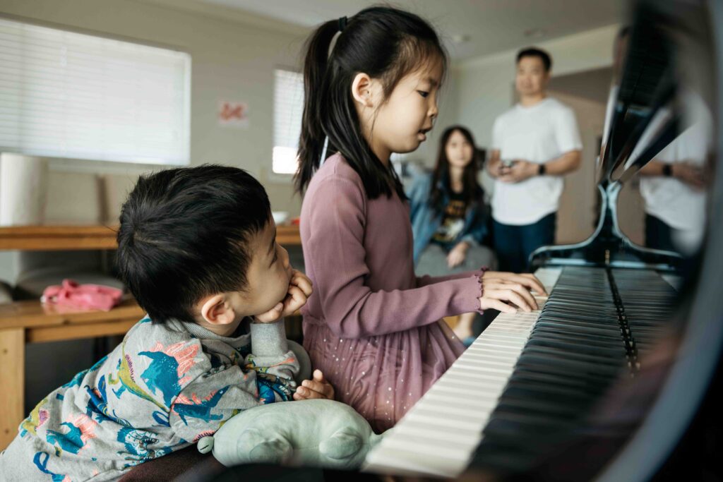 Younger sibling brother is looking up at his older sister adoringly as she plays the piano.