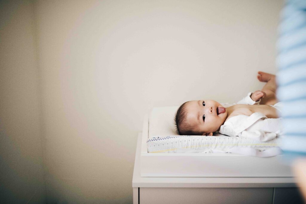 Young baby girl is sticking her tongue out on the changing table in her nursery at home.