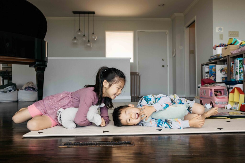 Young siblings are rolling on the floor while laughing during a family photo session.