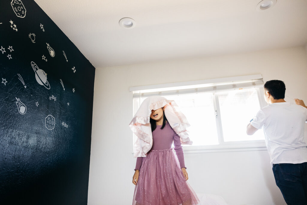 Girl is playing with a blanket over her head during a family photo session at home.