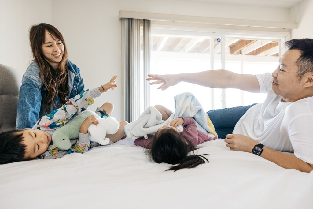 Dad and son are reaching for each other across the bed during a fun family photo session at home.