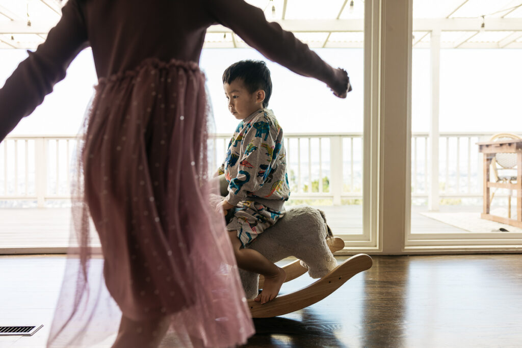 Toddler brother is rocking on an elephant rocking chair as his sister runs into the frame.
