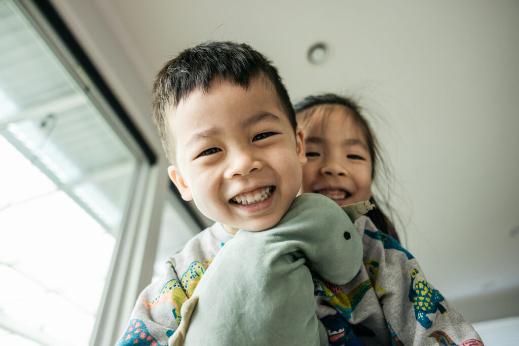 Young siblings are laughing while sharing the same rocking chair.