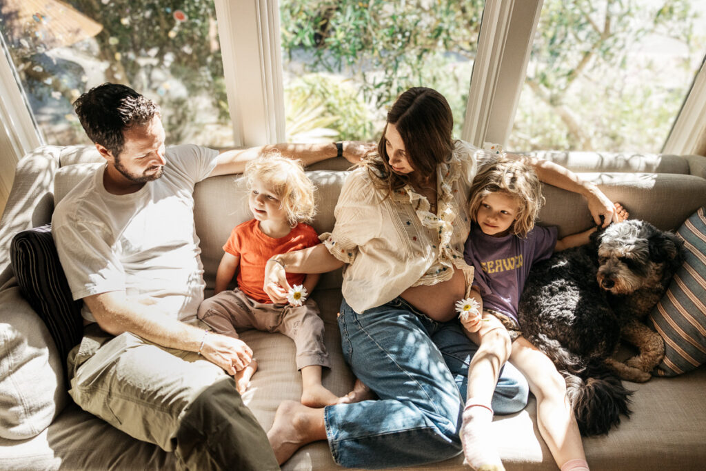 Entire family is cuddling on the sofa while holding daisies.