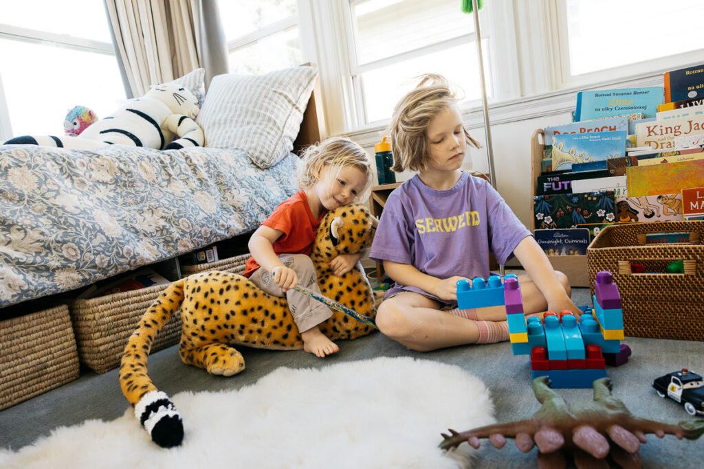 Young boys are playing with Mega Bloks, dinos, and a very large cheetah in their bedroom.