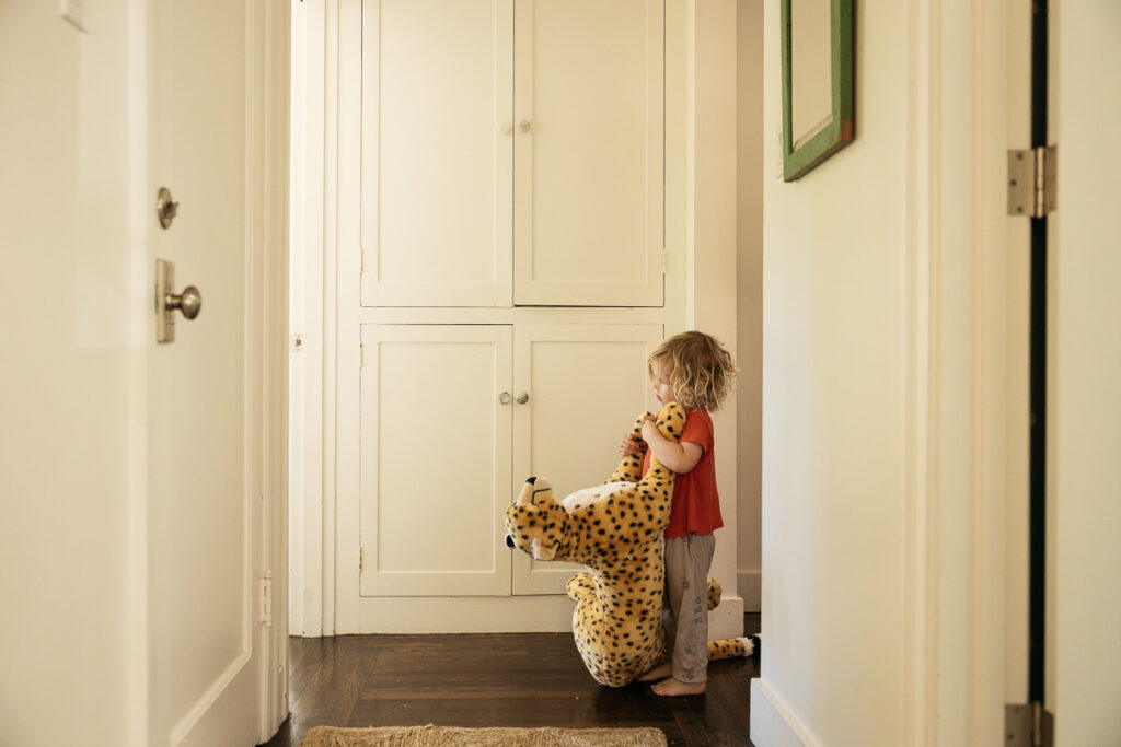 Toddler boy drags his large stuffed cheetah across the hardwood floors throughout the house.