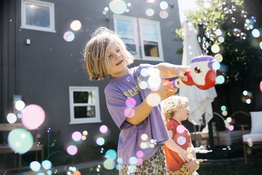 Young boy is blowing bubbles with a bubble gun in his backyard.